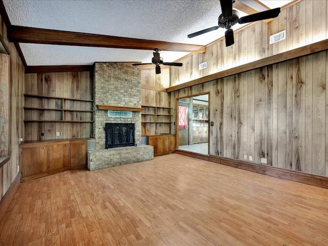 unfurnished living room featuring light wood-type flooring, a textured ceiling, wooden walls, and a brick fireplace