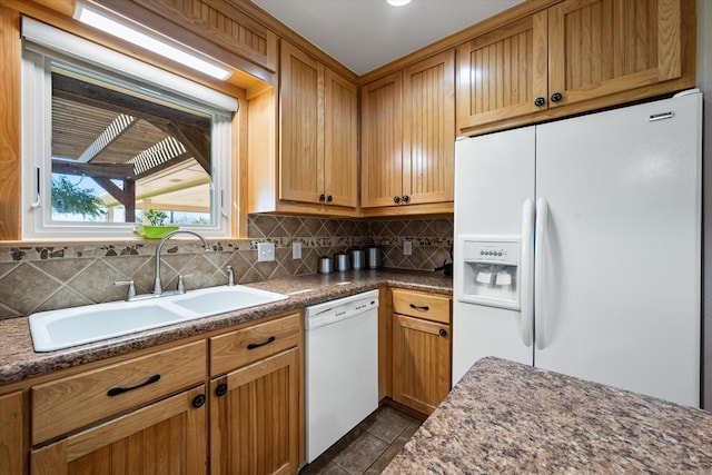 kitchen with tasteful backsplash, dark stone counters, white appliances, dark tile patterned floors, and sink