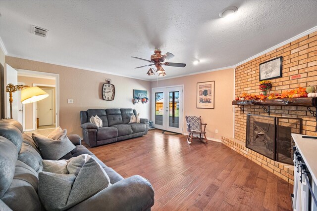 living room featuring crown molding, wood-type flooring, a textured ceiling, and a brick fireplace