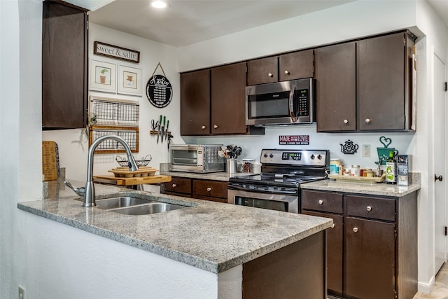 kitchen featuring sink, dark brown cabinetry, light stone countertops, kitchen peninsula, and stainless steel appliances