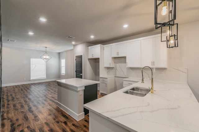 kitchen with pendant lighting, sink, white cabinets, light stone countertops, and a kitchen island