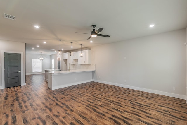 kitchen featuring ceiling fan with notable chandelier, pendant lighting, white cabinets, dark hardwood / wood-style flooring, and kitchen peninsula