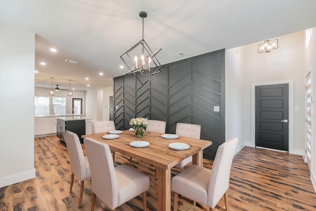 dining space featuring visible vents, an inviting chandelier, light wood-type flooring, a decorative wall, and recessed lighting