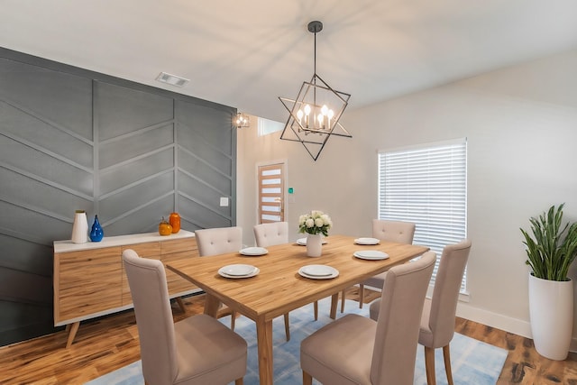 dining room featuring a notable chandelier, baseboards, visible vents, and wood finished floors