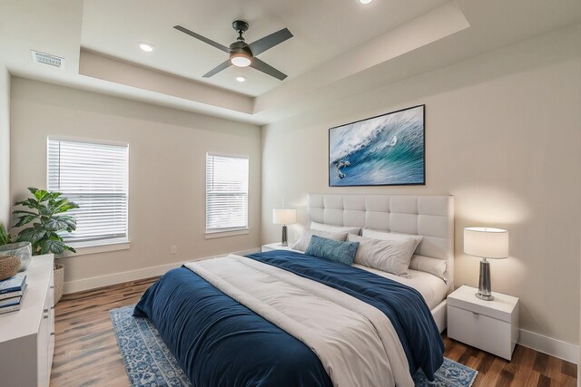 bedroom with ceiling fan, dark wood-type flooring, and a tray ceiling