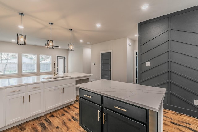 kitchen with light stone countertops, white cabinetry, a kitchen island with sink, sink, and decorative light fixtures