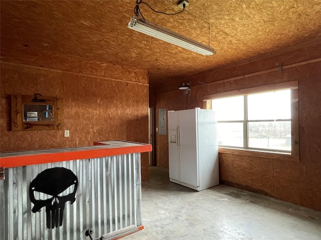 interior space featuring wood walls, electric panel, concrete floors, and white fridge with ice dispenser