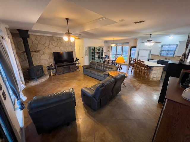 living room with ceiling fan, a raised ceiling, and a wood stove