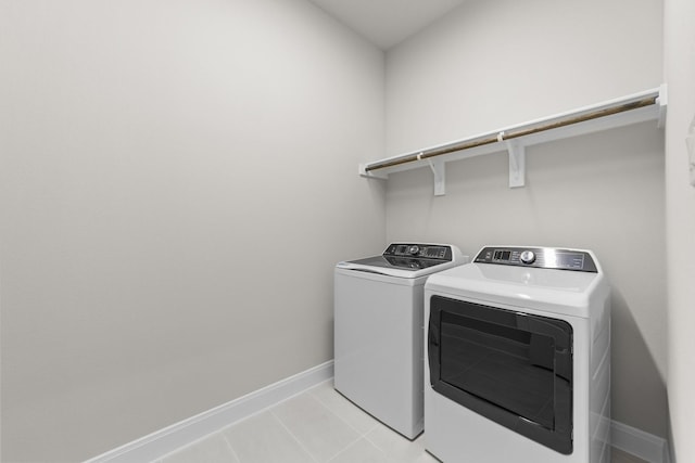 clothes washing area with laundry area, baseboards, washing machine and clothes dryer, and light tile patterned floors