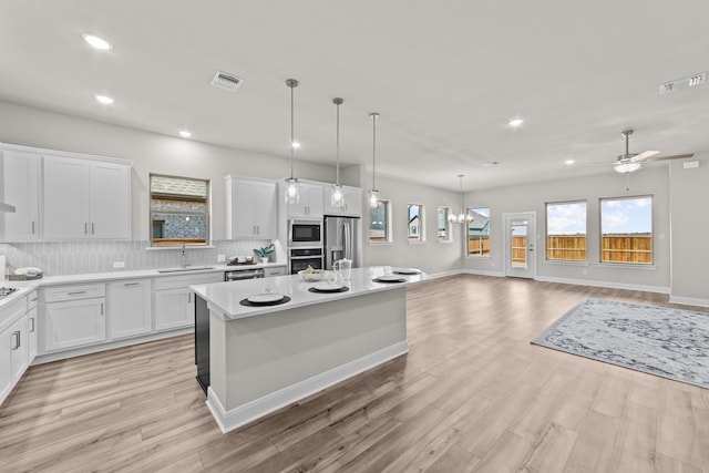 kitchen featuring a kitchen island, appliances with stainless steel finishes, open floor plan, light countertops, and white cabinetry