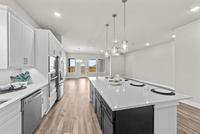 kitchen with appliances with stainless steel finishes, a kitchen island with sink, light countertops, and hanging light fixtures