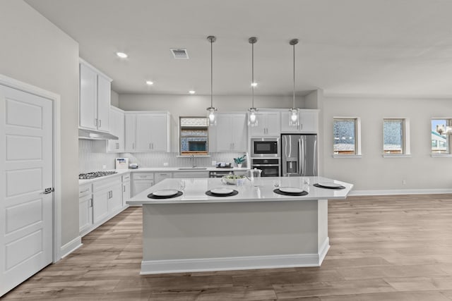 kitchen with stainless steel appliances, light countertops, a kitchen island with sink, and white cabinetry