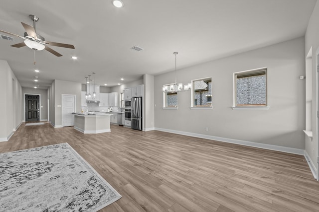 unfurnished living room featuring visible vents, baseboards, light wood-style flooring, ceiling fan with notable chandelier, and recessed lighting