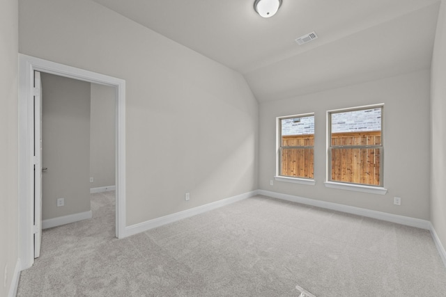 empty room featuring light carpet, baseboards, visible vents, and vaulted ceiling