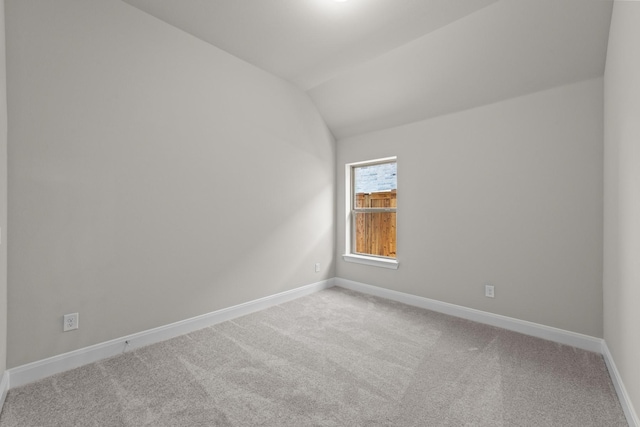 empty room with baseboards, vaulted ceiling, and light colored carpet