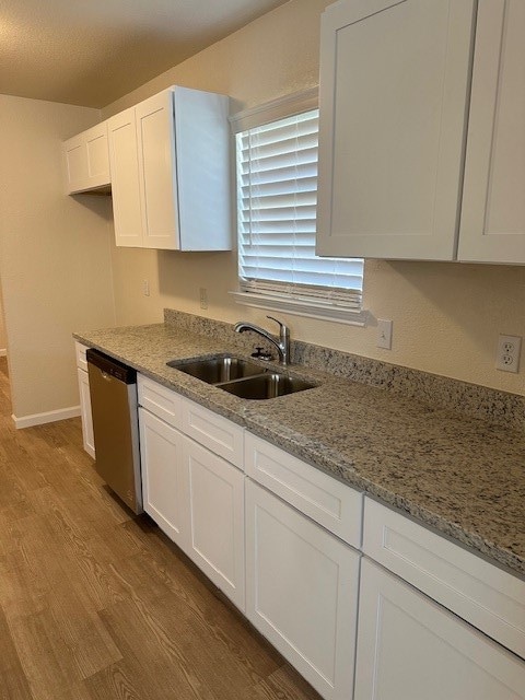 kitchen with light stone countertops, white cabinetry, dishwasher, sink, and light hardwood / wood-style floors