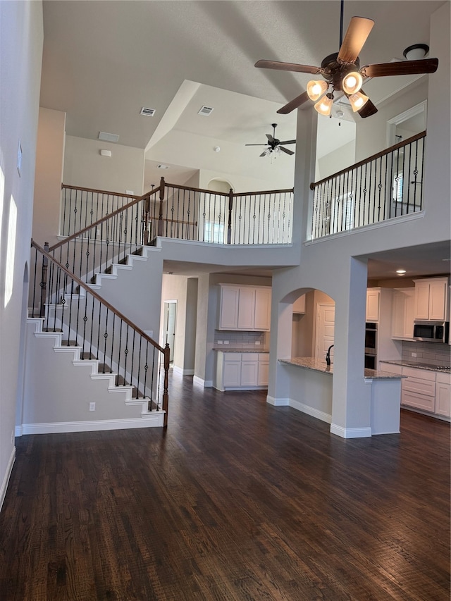 unfurnished living room with ceiling fan, dark hardwood / wood-style flooring, and a towering ceiling