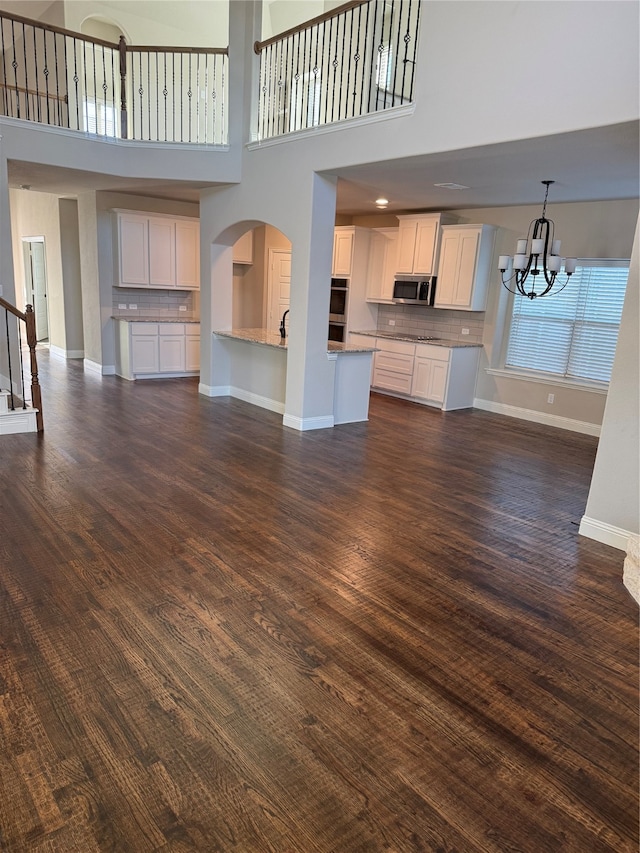 unfurnished living room with dark hardwood / wood-style flooring, a towering ceiling, and an inviting chandelier