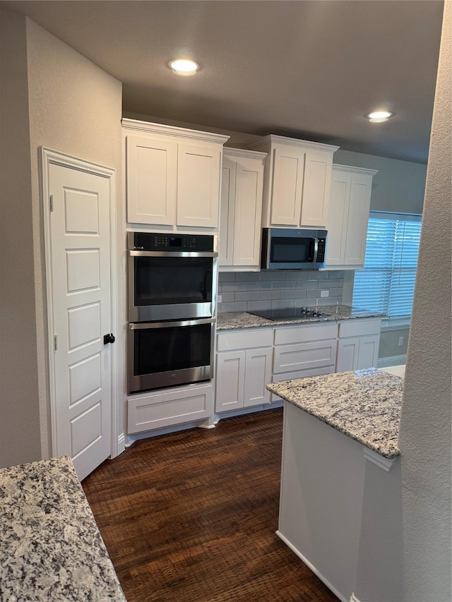 kitchen with light stone countertops, appliances with stainless steel finishes, tasteful backsplash, dark hardwood / wood-style flooring, and white cabinetry