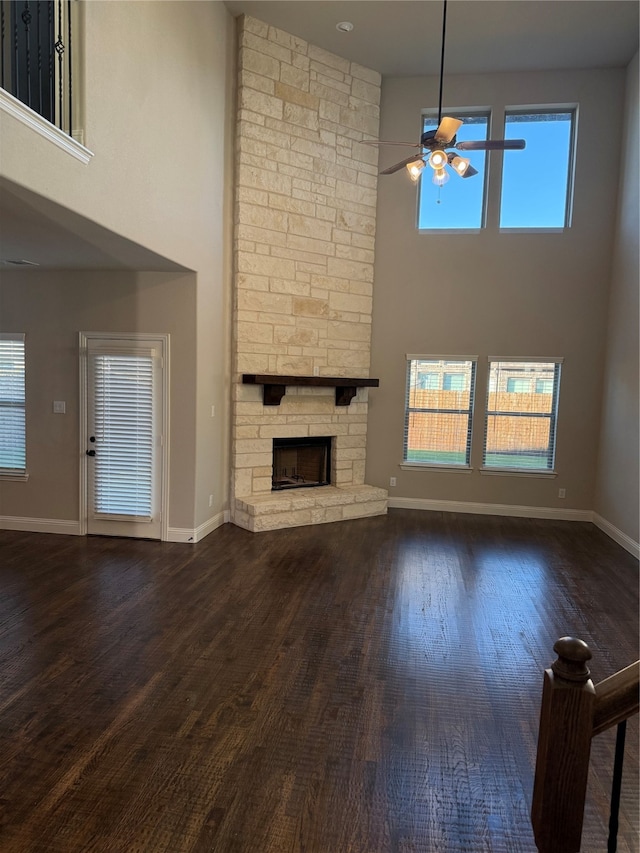 unfurnished living room featuring ceiling fan, a fireplace, dark wood-type flooring, and a high ceiling