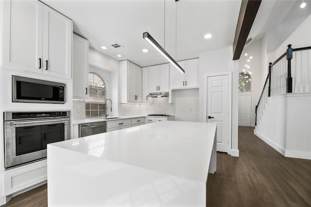 kitchen with appliances with stainless steel finishes, decorative light fixtures, white cabinets, a center island, and dark hardwood / wood-style floors