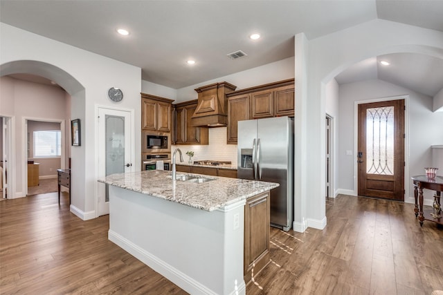 kitchen with sink, vaulted ceiling, appliances with stainless steel finishes, light stone countertops, and a kitchen island with sink