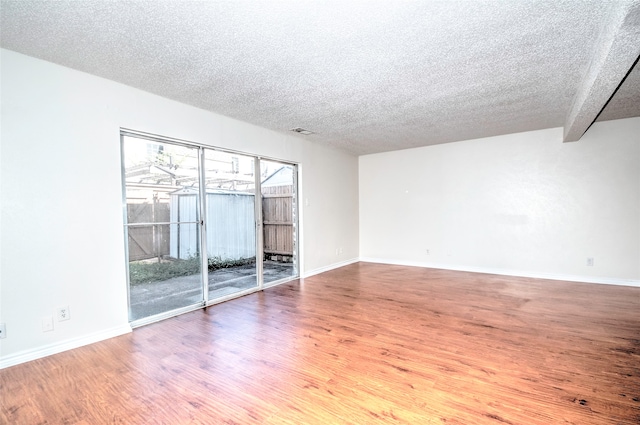 empty room featuring hardwood / wood-style flooring, beam ceiling, and a textured ceiling