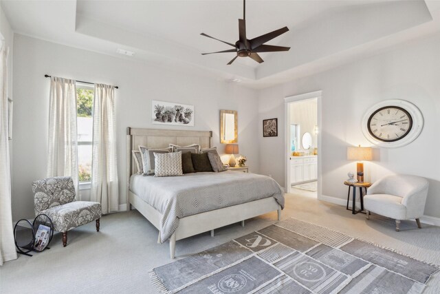 bedroom with ceiling fan, ensuite bathroom, and a tray ceiling