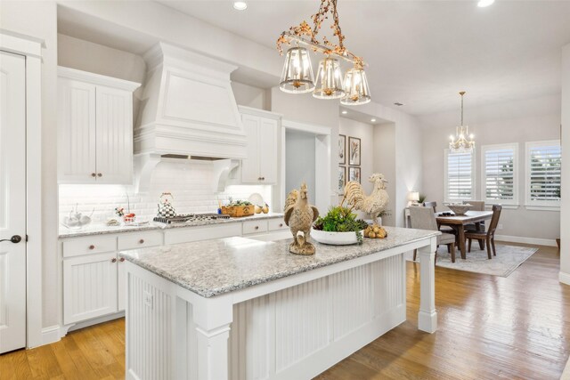 kitchen featuring white cabinetry, a kitchen island with sink, pendant lighting, light hardwood / wood-style floors, and decorative backsplash