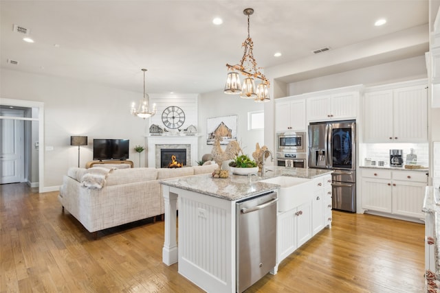 kitchen with stainless steel appliances, sink, light hardwood / wood-style flooring, white cabinetry, and an island with sink