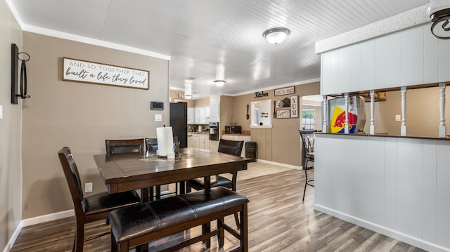 dining area with light hardwood / wood-style floors, ornamental molding, and wood walls