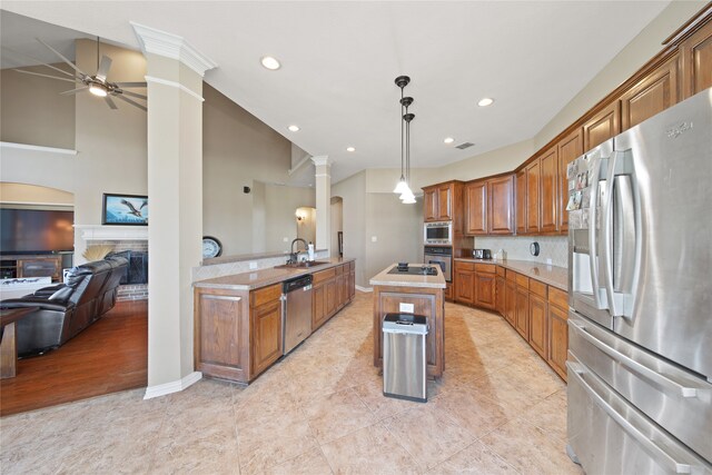 kitchen featuring sink, stainless steel appliances, decorative columns, pendant lighting, and a kitchen island with sink