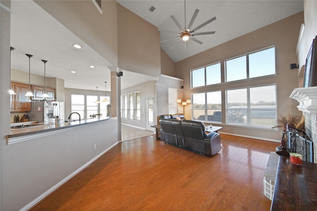 living room with ceiling fan, a brick fireplace, decorative columns, a towering ceiling, and hardwood / wood-style flooring