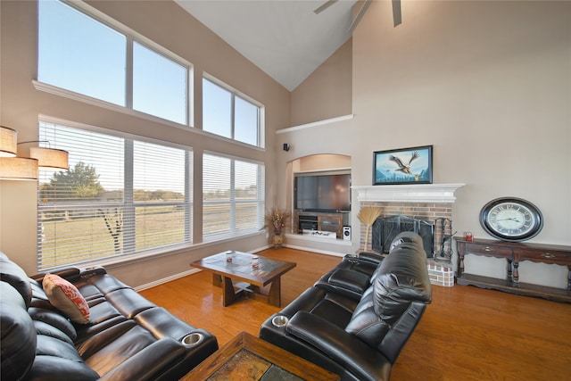 living room with ceiling fan, high vaulted ceiling, wood-type flooring, and a brick fireplace