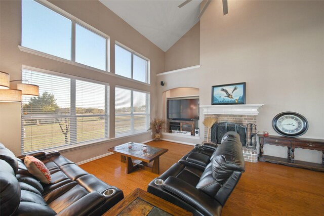 living room with ceiling fan, high vaulted ceiling, wood-type flooring, and a brick fireplace