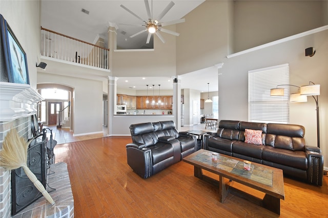 living room with a high ceiling, ceiling fan, light wood-type flooring, a fireplace, and decorative columns