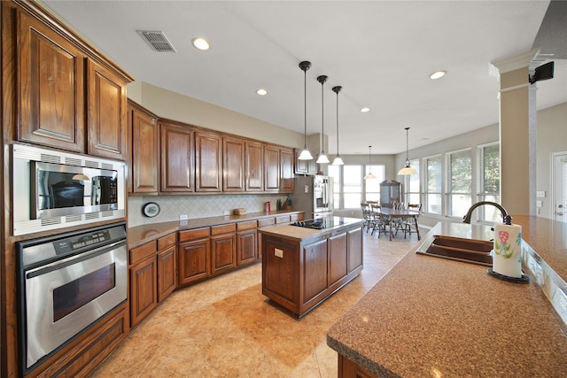 kitchen with pendant lighting, a center island with sink, sink, ornate columns, and appliances with stainless steel finishes