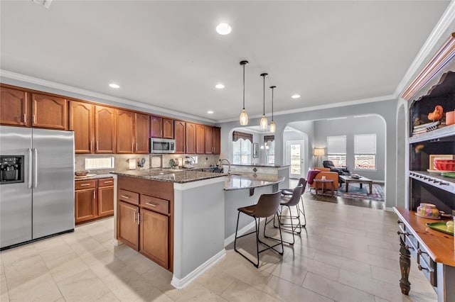 kitchen with hanging light fixtures, stainless steel appliances, crown molding, an island with sink, and stone countertops