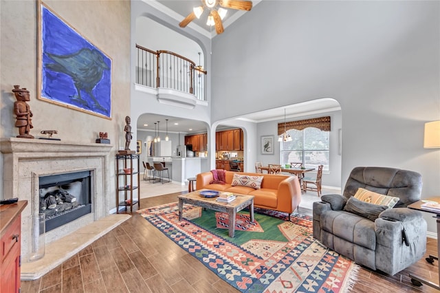 living room with a towering ceiling, light hardwood / wood-style floors, ceiling fan with notable chandelier, and ornamental molding