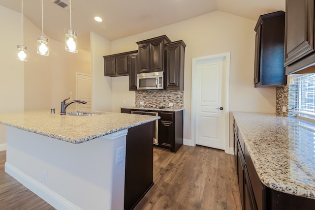 kitchen with light stone countertops, dark hardwood / wood-style flooring, vaulted ceiling, sink, and pendant lighting