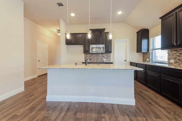 kitchen with decorative backsplash, an island with sink, dark wood-type flooring, and lofted ceiling