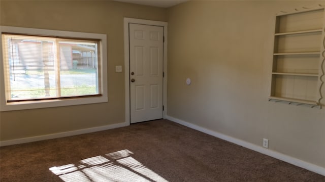 empty room featuring dark colored carpet and built in shelves