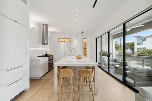 kitchen featuring white cabinets, a kitchen breakfast bar, high end stainless steel range, light wood-type flooring, and extractor fan