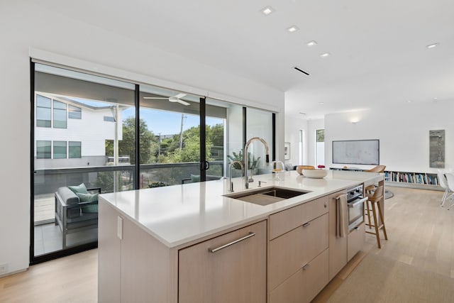 kitchen featuring a breakfast bar, sink, light hardwood / wood-style floors, a kitchen island with sink, and light brown cabinetry