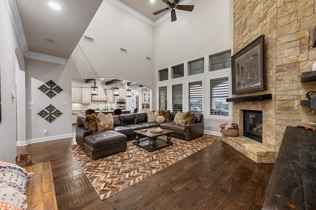 living room with ceiling fan, ornamental molding, a fireplace, and a towering ceiling