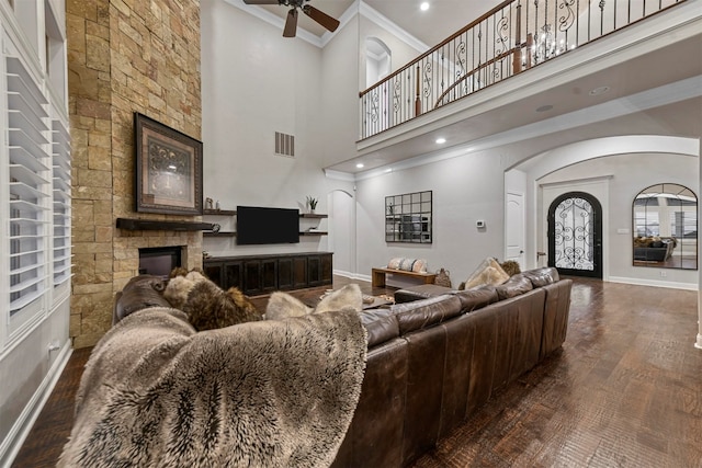 living room with dark hardwood / wood-style flooring, ceiling fan, crown molding, a fireplace, and a high ceiling