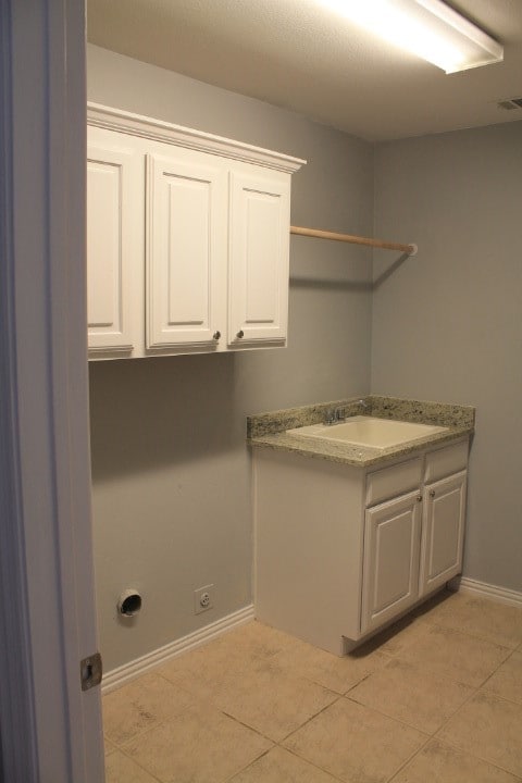 clothes washing area featuring hookup for an electric dryer, light tile patterned flooring, cabinets, and sink