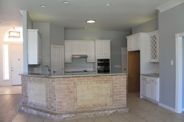 kitchen with white cabinetry, light stone countertops, double oven, backsplash, and light tile patterned floors