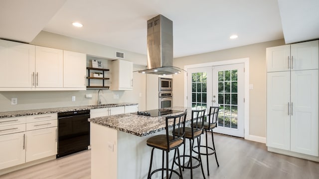 kitchen with island exhaust hood, stone counters, white cabinets, and black appliances