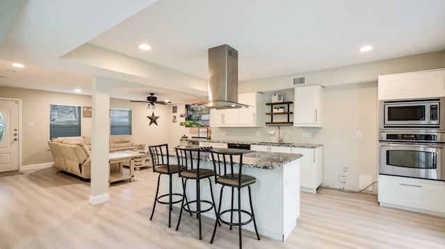 kitchen with island exhaust hood, white cabinets, dark stone counters, and appliances with stainless steel finishes